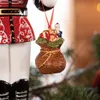 A close-up of a Christmas ornament hanging from a tree, featuring a sack of gifts with a teddy bear and Santa Claus figurine. Podgląd zdjęcia produktu