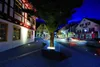 A street scene at night with buildings and a tree. Produktbild-Vorschau