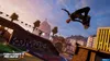 A skateboarder performing a trick in a skate park with a city skyline in the background. Produktbild-Vorschau