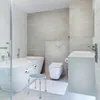 A modern, clean bathroom with a bathtub, toilet, and sink. A shower stool and a grab bar are placed in the scene. Náhľad obrázku produktu