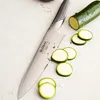 A chef's knife is shown next to sliced zucchini on a light-colored surface. Anteprima dell’immagine prodotto