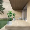 A modern outdoor patio with wooden decking, featuring two potted plants, a chair, and a glass door leading indoors. Náhľad obrázku produktu