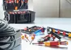 A collection of electrical tools laid out on a metallic surface, with a toolbox in the background. Podgląd zdjęcia produktu