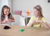 Two young girls are playing with toys on a wooden table. Produktbild-Vorschau
