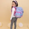 A young girl wearing a backpack and standing in front of a light yellow background with balloons. Produktbild-Vorschau