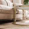A close-up view of a round coffee table with a gold frame and a marble top, placed in front of a beige sofa. Produktbild-Vorschau