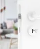 A close-up view of a white door handle and lock mechanism, with a blurred interior scene visible through the open door. Produktbild-Vorschau