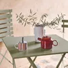 A table setting on a patio with a teapot, mug, and plant. Produktbild-Vorschau