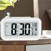 A digital alarm clock is displayed on a wooden surface, with a plant in the background. Voir les images du produit
