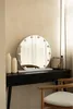 A vanity mirror with lights sits on a black dresser, next to two white vases and some cosmetic bottles. A wooden chair is partially visible in the foreground. Náhled obrázku produktu
