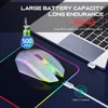 A white wireless mouse with colorful RGB lighting is placed on a black mousepad next to a laptop. A charging cable is connected to the mouse. Produktbild-Vorschau