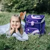 A young girl is lying on the grass next to a backpack. Produktbild-Vorschau