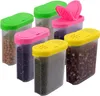 A group of six clear plastic spice containers with colorful lids (green, pink, and yellow) filled with various grains and seeds, arranged on a white background. Produktbild-Vorschau