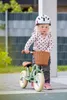 A young child wearing a helmet stands next to a balance bike with a basket. Produktbild-Vorschau