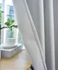 A close-up view of a textured gray curtain with a subtle herringbone pattern, partially obscuring a window and a small white cup and saucer on a book. Produktbild-Vorschau