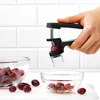 A hand is using a cherry pitter to remove the pit from a cherry over a bowl of pitted cherries. Another bowl of cherries is visible in the background. Anteprima dell’immagine prodotto