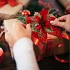 Hands decorating a Christmas gift with a red and gold poinsettia ornament. Produktbild-Vorschau