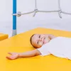 A young boy is lying on a yellow mat, smiling. Voir les images du produit
