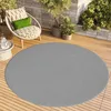A round gray rug on a wooden deck with outdoor furniture and plants.