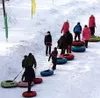 People are walking up a snowy slope, pulling inflatable tubes. Produktbild-Vorschau
