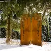 A decorative metal screen with a floral pattern stands in a snowy garden setting, partially obscured by a large evergreen tree. Produktbild-Vorschau