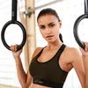 A woman is holding onto gymnastic rings in a gym. Produktbild-Vorschau