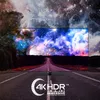A television displaying a vibrant space scene is placed on a road, with a cosmic sky in the background. A circular logo with text is in the foreground. Produktbild-Vorschau