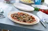 A pizza is served on a plate on a table, with other plates and ingredients in the background. Produktbild-Vorschau