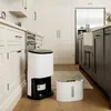 A white dehumidifier and air purifier is shown in a modern kitchen with white cabinets and dark gray island cabinets. Náhled obrázku produktu