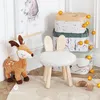 A children's room setup with a deer plush toy, a fluffy stool with bunny ears, and a stack of decorative storage boxes adorned with woodland animal illustrations and fairy lights. Produktbild-Vorschau