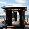A cabana with black curtains and cushions on a beach with the ocean and sky in the background. Voir les images du produit