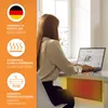A woman is working on her laptop at a desk, with a desk heater warming her legs. Produktbild-Vorschau