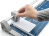 A hand is using a paper trimmer to cut a piece of white paper. Voir les images du produit