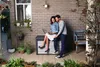A couple is sitting on a storage box on a patio, looking at a laptop. Podgląd zdjęcia produktu