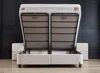 A beige boxspring bed with its storage compartment open, revealing the internal mechanism. Two beige nightstands are visible on either side. Produktbild-Vorschau