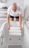 A man is placing a white bath stool into a bathtub. Produktbild-Vorschau