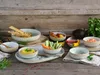A collection of ceramic bowls and plates filled with various dips, crackers, and vegetables, arranged on a rustic wooden surface. Produktbild-Vorschau