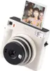 A white Fujifilm instax SQUARE SQ 1 instant camera with a photo sticking out of the top. Produktbild-Vorschau