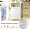 A white bathroom cabinet with a door and an open shelf above, placed near a window with a city view. The background is a textured wall. Below the cabinet, icons and text indicate product features. Produktbild-Vorschau