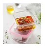 Two glass food containers stacked on a white surface, with herbs and peppercorns scattered around. Produktbild-Vorschau