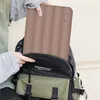 A person is putting a brown laptop sleeve into a backpack. Produktbild-Vorschau
