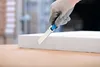 A gloved hand is using a utility knife to cut a piece of white insulation material. Voir les images du produit