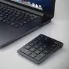 A black wireless numpad is placed next to a black laptop on a light gray surface. Náhled obrázku produktu