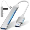 A silver USB hub with four blue USB ports and a white cable connected to a USB 3.0 connector. A small black USB drive is attached to the hub via a short white cable. Produktbild-Vorschau