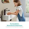 A young girl is washing her hands at a wall-mounted sink. Produktbild-Vorschau
