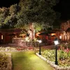 A courtyard at night with a large tree, garden lights, and outdoor seating. Produktbild-Vorschau