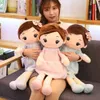 A woman is holding three plush dolls. The dolls are dressed in dresses and have brown hair with bows. Náhled obrázku produktu