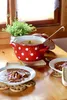 A red and white polka dot pot filled with food sits on a wooden table, with two bowls of food and a plant in the background. Anteprima dell’immagine prodotto