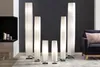 A collection of tall, white, pleated floor lamps are arranged in a modern living room setting. Produktbild-Vorschau
