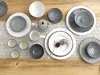 A collection of ceramic dishes and a teapot arranged on a wooden table with a lace runner. Produktbild-Vorschau